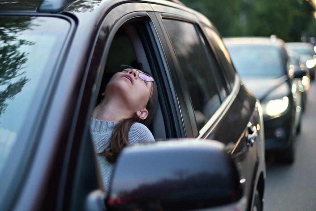 A young woman stands in a traffic jam and looks out through the window trying to discern the cause of the traffic jam. rush hour